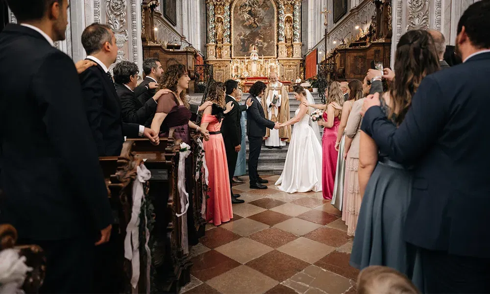 Blick auf das Brautpaar während der Zeremonie in einer prunkvollen Kirche, eingerahmt von Gästen in festlicher Kleidung.