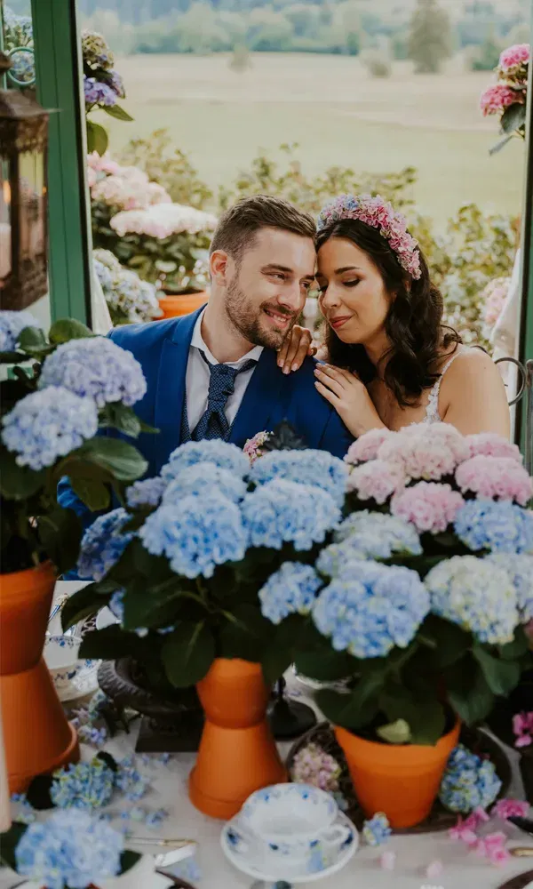 Braut und Bräutigam genießen einen romantischen Moment zwischen üppigen Hortensien in Tontöpfen.