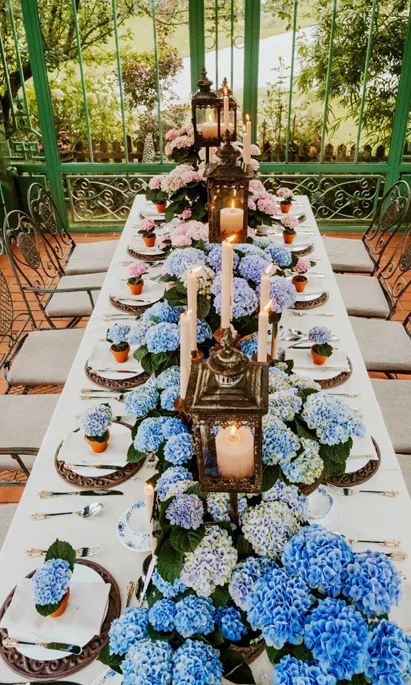 Elegante DIY-Hochzeitstischdeko mit üppigen Topf-Hortensien in Blau und stimmungsvollen Kerzen in Metalllaternen.