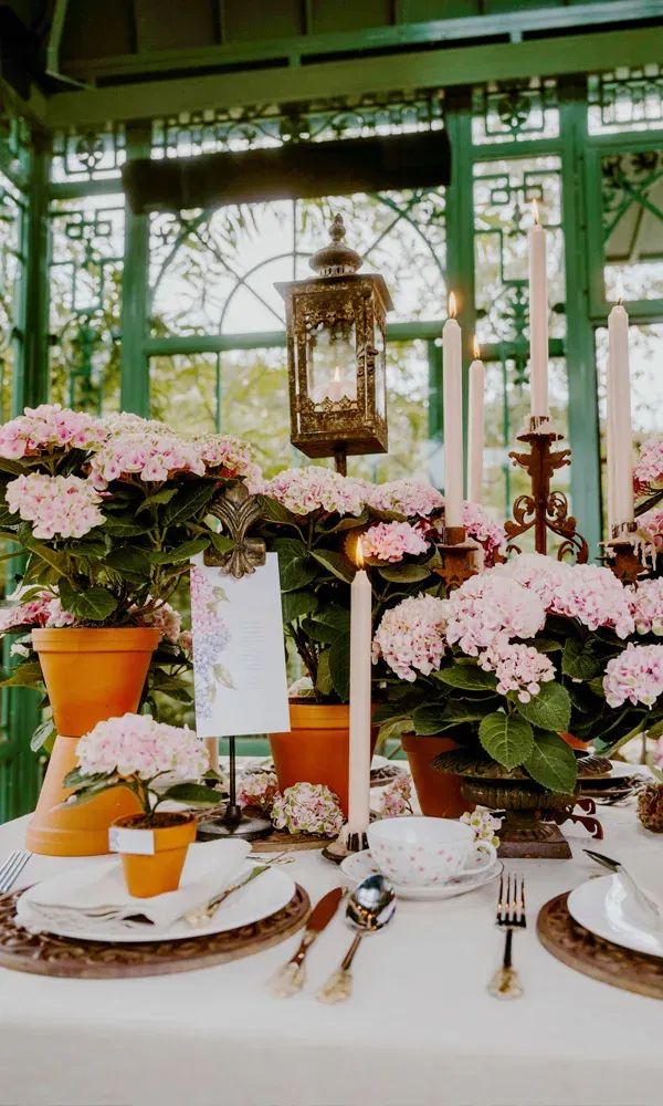DIY-Tischdeko mit pinkfarbenen Hortensien, weißen Kerzen und liebevoll gedeckten Tellern im Grünen.