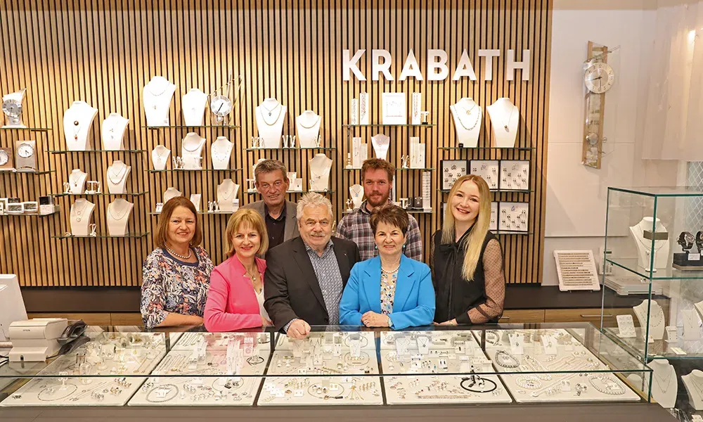 Teamfoto der Mitarbeitenden des Juweliergeschäfts Krabath vor der Schmuckauslage im Laden.