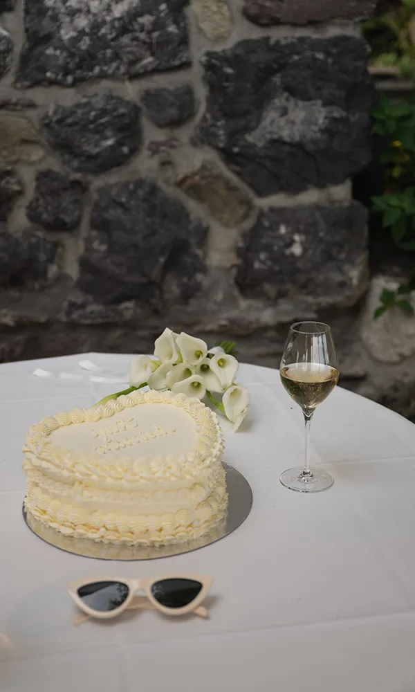 Hochzeitstorte in Herzform auf dem Tisch mit Calla-Blumen, Champagnerglas und Sonnenbrille als Accessoire.