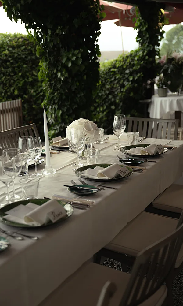 Elegant gedeckter Tisch für die Hochzeitsfeier im Freien mit weißen Blumen, Kerzen und Namenskärtchen.