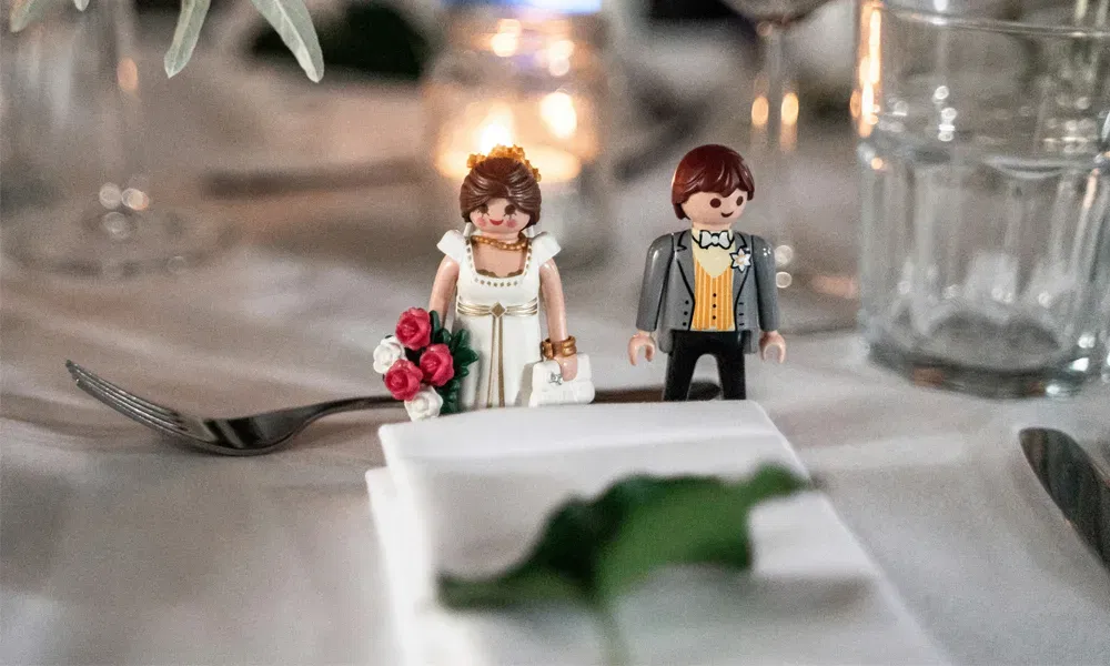 Verspielte Tischdeko zur Hochzeit mit Playmobil-Figuren als Braut und Bräutigam, vor einer stimmungsvoll gedeckten Tafel mit Kerzen und Gläsern.
