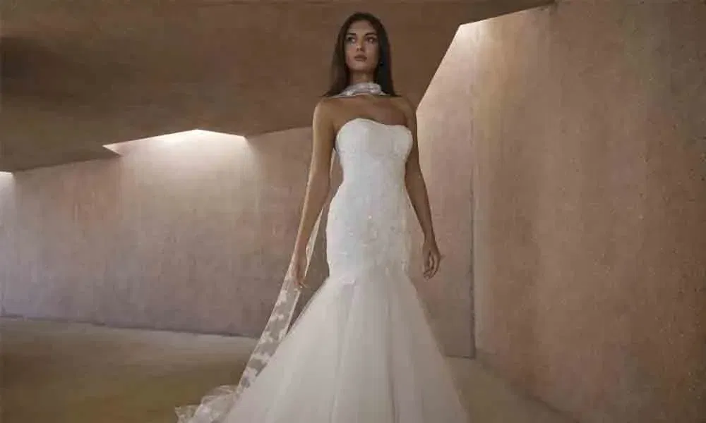 Modernes Mermaid-Hochzeitskleid mit figurbetontem Schnitt, Spitzenapplikationen und fließender Schleppe in einem minimalistischen Raum.