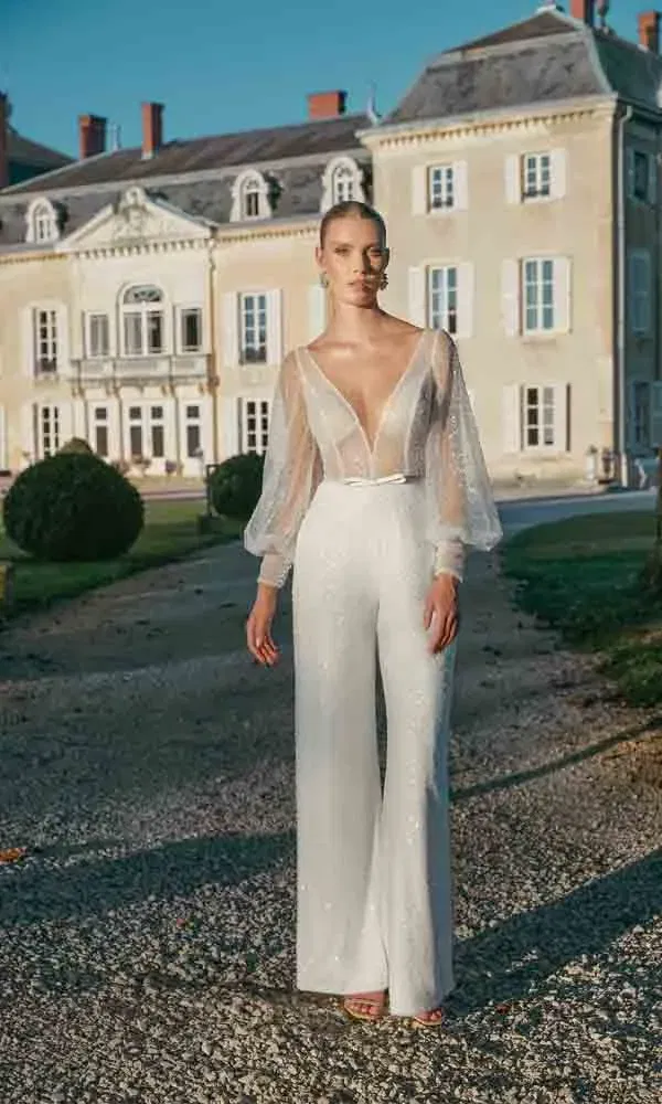 Stilvolle Hochzeitsaufnahme: Frau im modernen Braut-Jumpsuit mit weiten Hosenbeinen und Ballonärmeln im Schlossgarten.