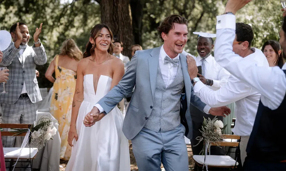 Braut und Bräutigam ziehen strahlend an ihren Gästen vorbei, die gratulieren und applaudieren – lebendiger Moment nach der Trauung.