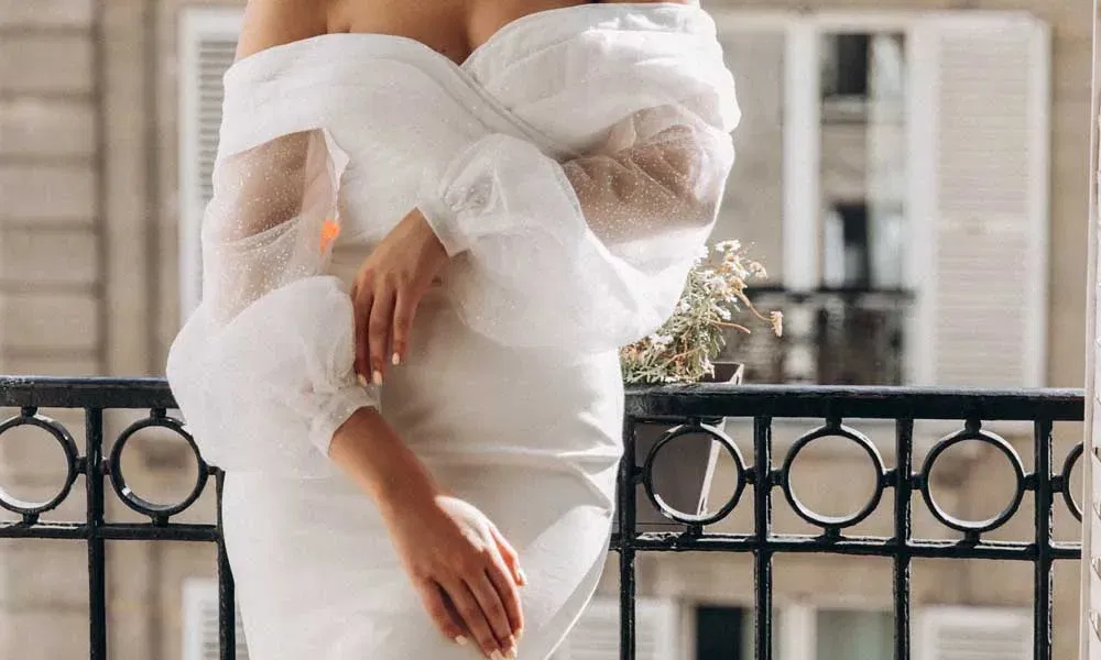 Detailaufnahme einer Braut in einem modernen, figurbetonten Kleid mit Tüllärmeln vor Pariser Architektur