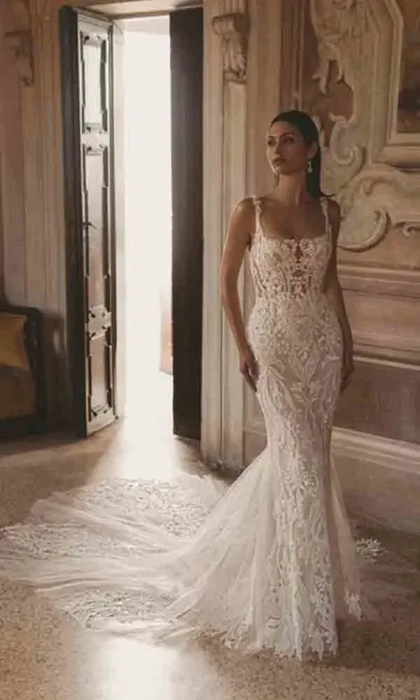 Elegantes Brautkleid mit aufwendigem Spitzenmuster und figurbetonter Silhouette, fotografiert im lichtdurchfluteten historischen Innenraum.