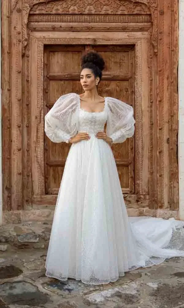 Elegantes Brautkleid mit verspielten voluminösen Ärmeln – inszeniert vor geschnitzter Tür.