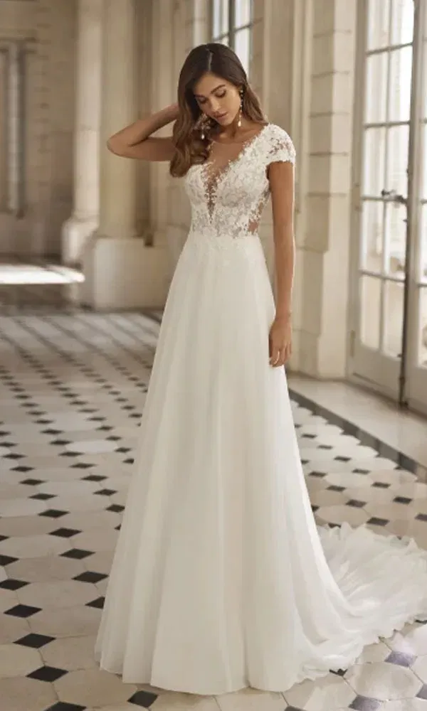 Zartes Brautkleid mit tiefem V-Ausschnitt, floraler Spitze und fließendem Rock – Braut schaut nach unten und berührt ihr Haar.