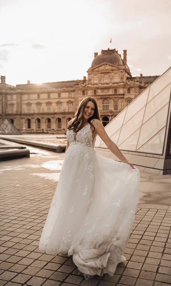 Strahlende Braut mit Babybauch dreht sich vor den Pyramiden des Louvre im Abendlicht.