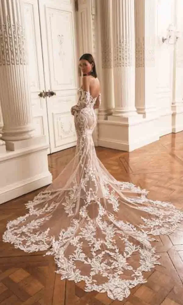 Figurbetontes Brautkleid mit off-shoulder-Trägern und kunstvoller Spitzenstickerei, die sich über eine lange Tüllschleppe erstreckt.