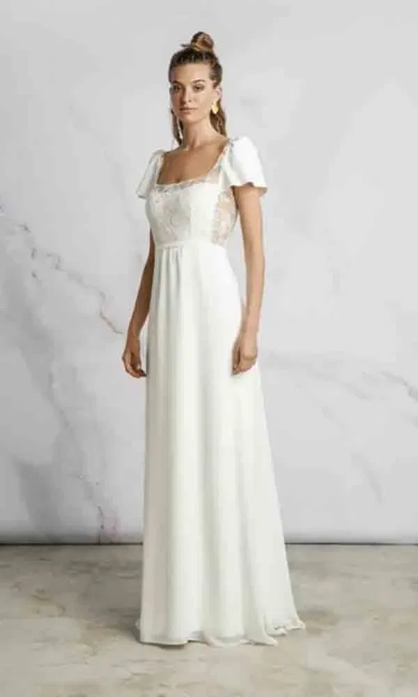 Weißes Hochzeitskleid mit verspielter Spitze und weitem Rock – das Modell posiert in schlichter Studio-Umgebung.