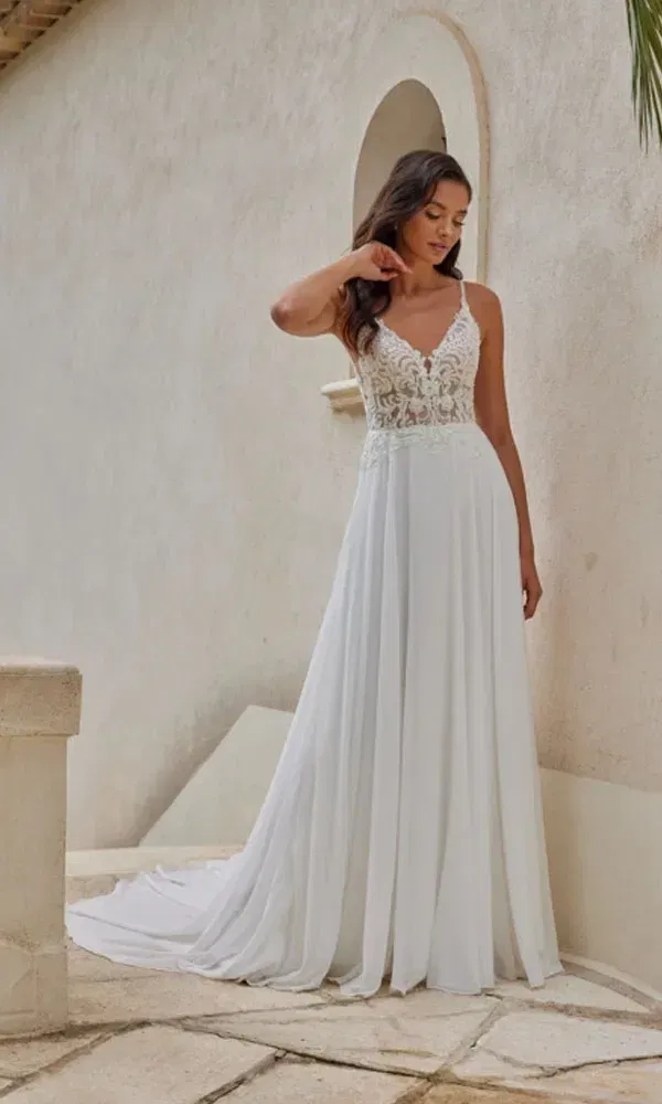 Sommerliches Hochzeitskleid mit zarten Trägern, floraler Spitze und fließendem Chiffonrock – Braut steht entspannt im Freien.