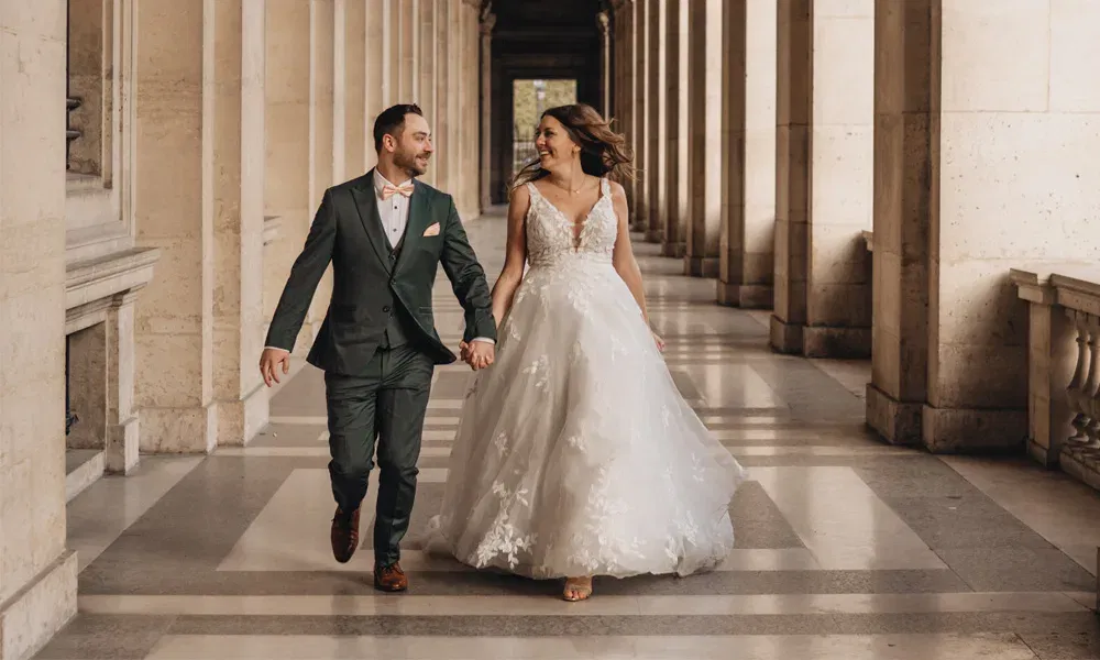 Fröhliche Szene: Bräutigam und schwangere Braut gehen gemeinsam durch die eleganten Säulengänge des Louvre.