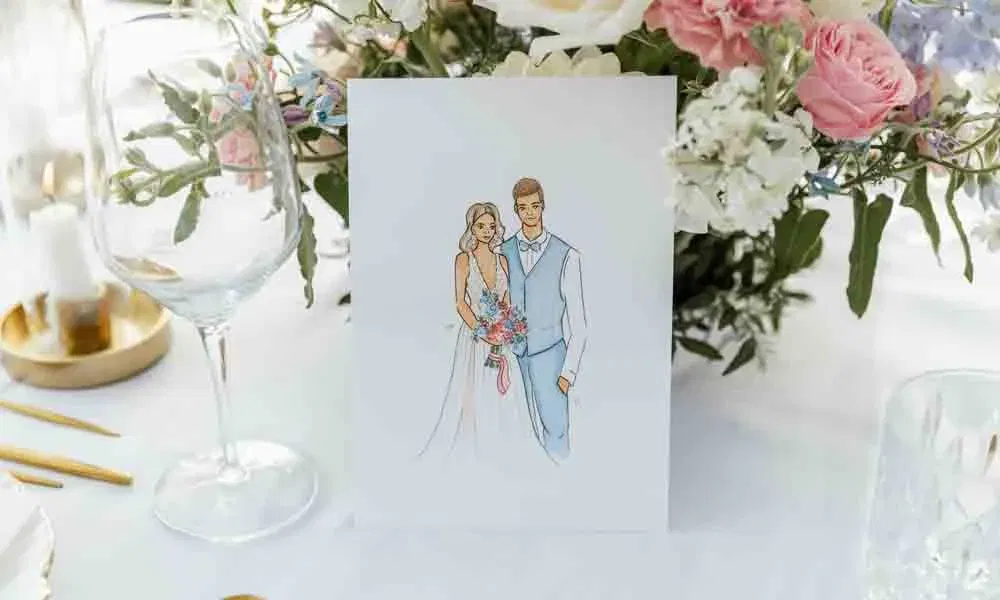 Detailaufnahme einer gezeichneten Hochzeitskarte mit Brautpaar-Motiv, liebevoll arrangiert zwischen Pastellblumen und Gläsern.