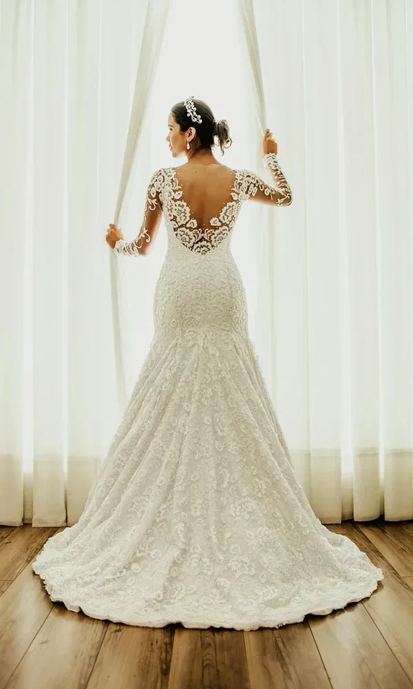 Rückansicht einer Braut mit langärmligem Spitzenbrautkleid und opulenter Schleppe im Tageslicht.
