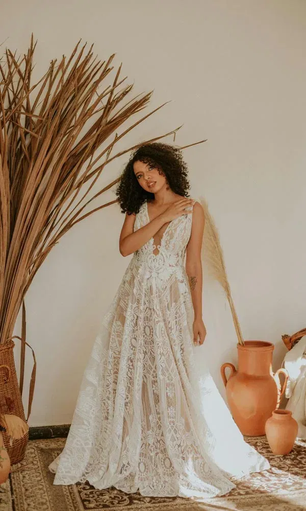 Stilvolle Boho-Hochzeitsaufnahme: Braut in tief ausgeschnittenem Spitzenkleid in rustikal dekorierter Ecke.