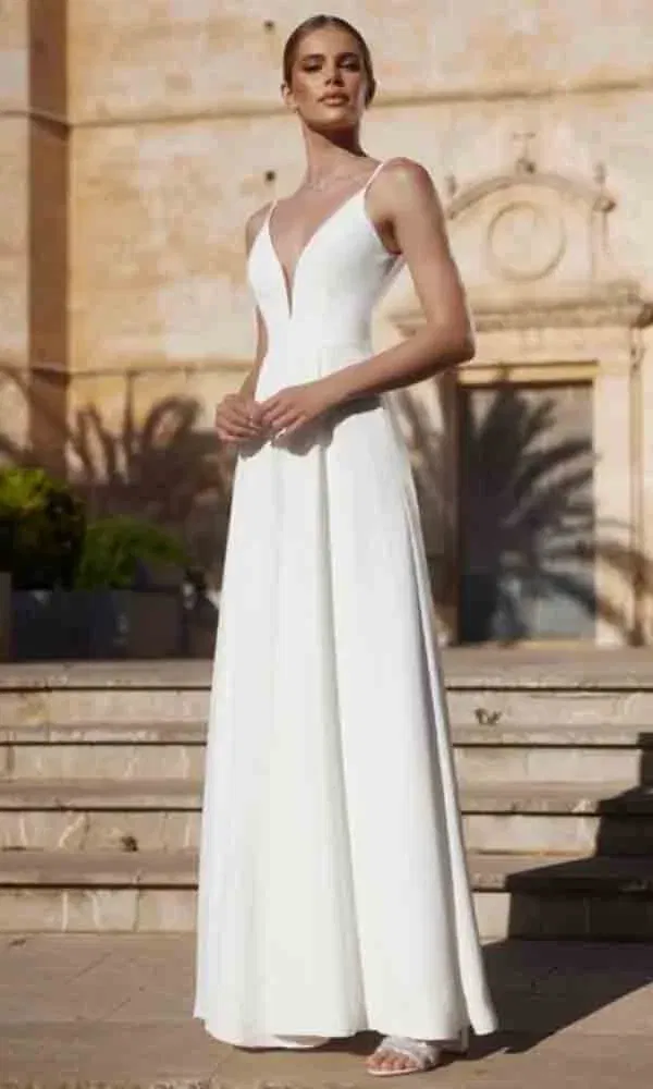 Schlichter und eleganter Hochzeitslook: Frau in einem Braut-Jumpsuit mit Spaghettiträgern und femininer Silhouette.