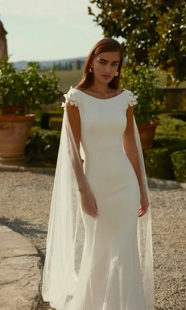 Elegantes Fit-and-Flare-Kleid mit fließendem Tüllcape – Braut mit glattem Haar in toskanischer Kulisse.
