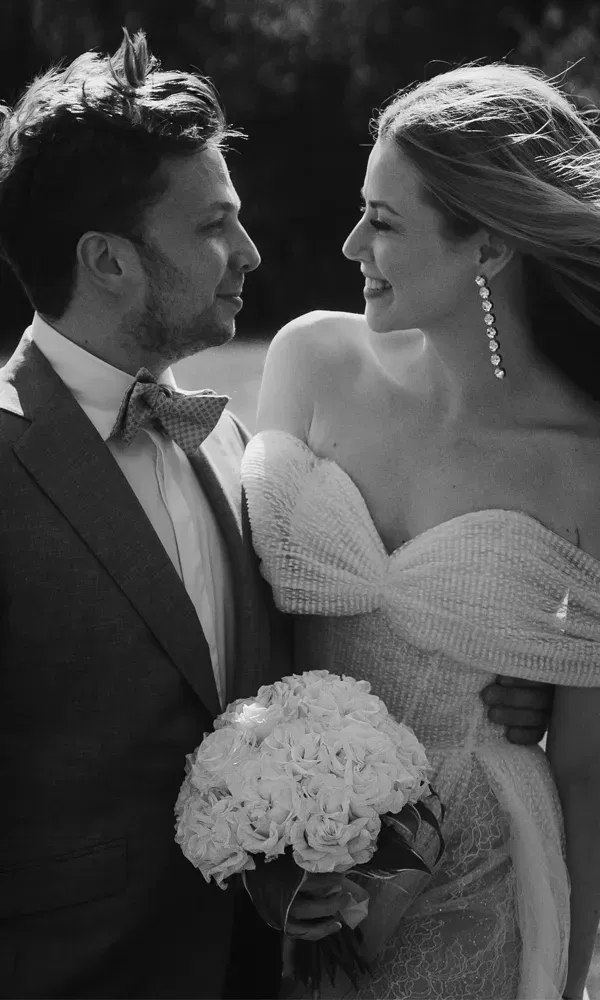 Verträumter Moment in Schwarz-Weiß: Das Paar schaut sich innig an, die Braut trägt ein schulterfreies Kleid und hält Blumen.