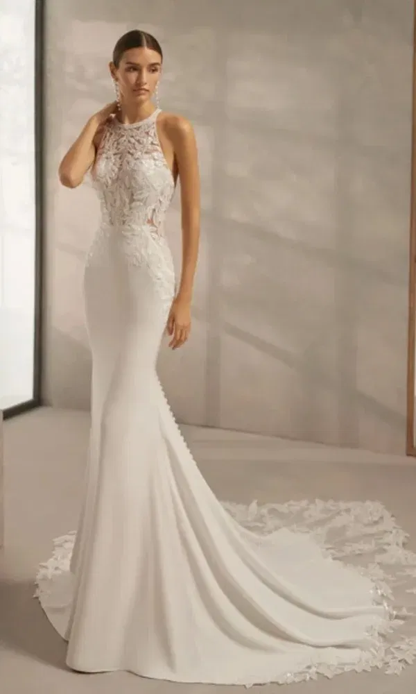 Elegantes Meerjungfrau-Brautkleid mit floraler Spitze und hoher Halslinie, getragen von einer Braut mit zurückgebundenem Haar.