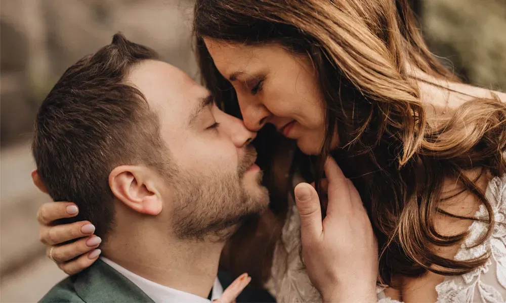 Nahaufnahme eines verliebten Paares im Hochzeitslook, das sich sanft berührt und emotional verbunden ist.