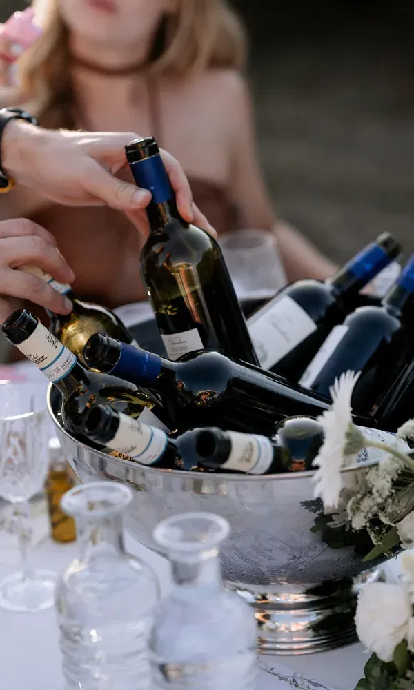 Detailaufnahme einer Metallkühlwanne mit italienischen Weinen auf einer Hochzeitstafel – lebendige Stimmung im Hintergrund.