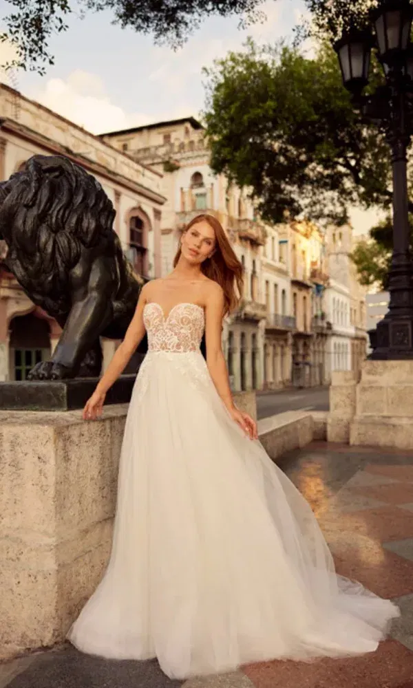 Romantisches Brautkleid mit tiefem Ausschnitt und zarter Stickerei vor urbaner Kulisse mit Löwenfigur.