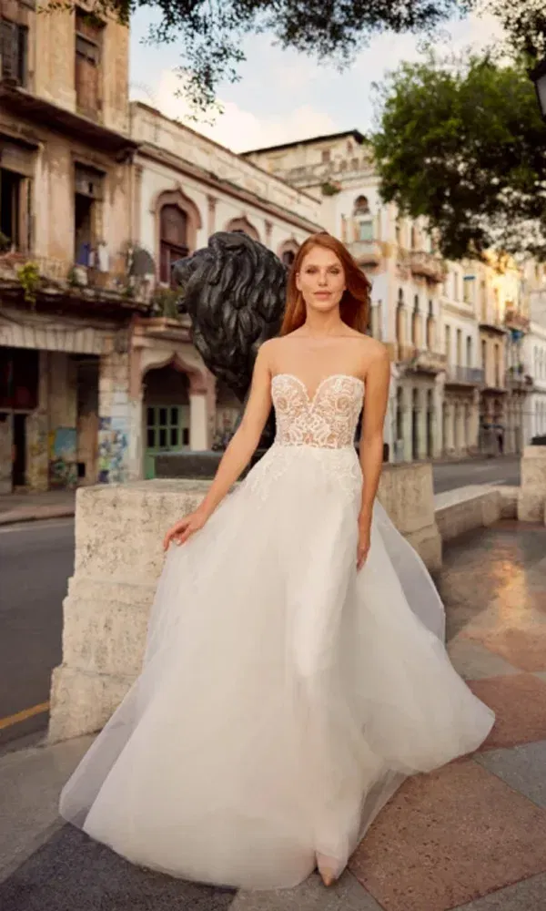 Elegante Frau in trägerlosem Hochzeitskleid mit Herz-Ausschnitt spaziert durch eine alte Stadtstraße.