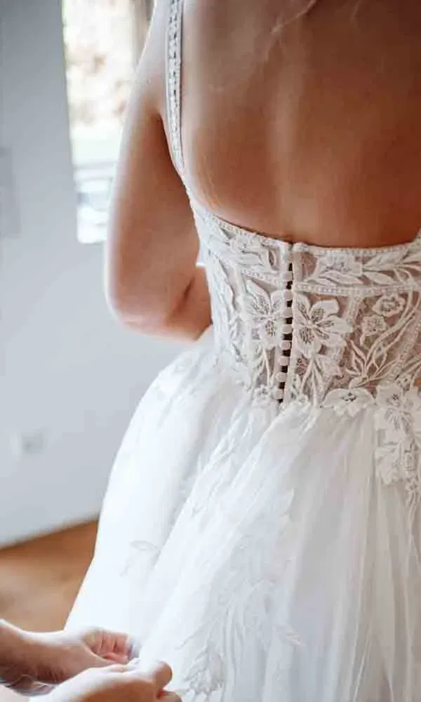 Detailansicht der Knöpfe und Spitzenverzierung auf dem Rücken des Brautkleids kurz vor der Hochzeit.