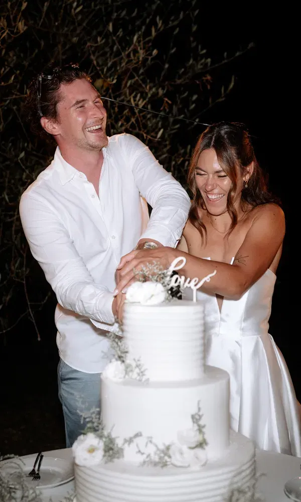 Glücklicher Moment beim Tortenanschnitt: Braut und Bräutigam lachen herzlich beim ersten Schnitt in die Hochzeitstorte.