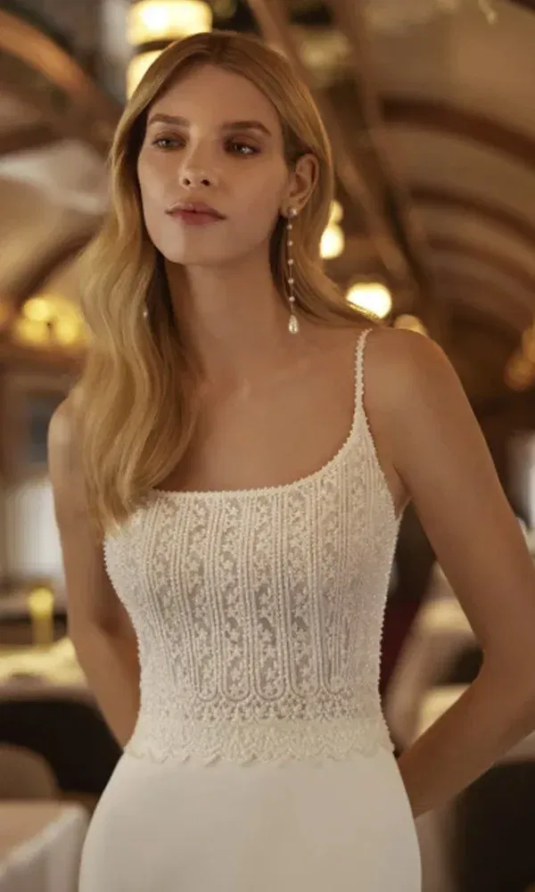 Braut mit offenen, welligen Haaren trägt ein figurbetontes Brautkleid mit feiner Spitze am Oberteil und schmalen Trägern, aufgenommen in stilvollem Retro-Zug.
