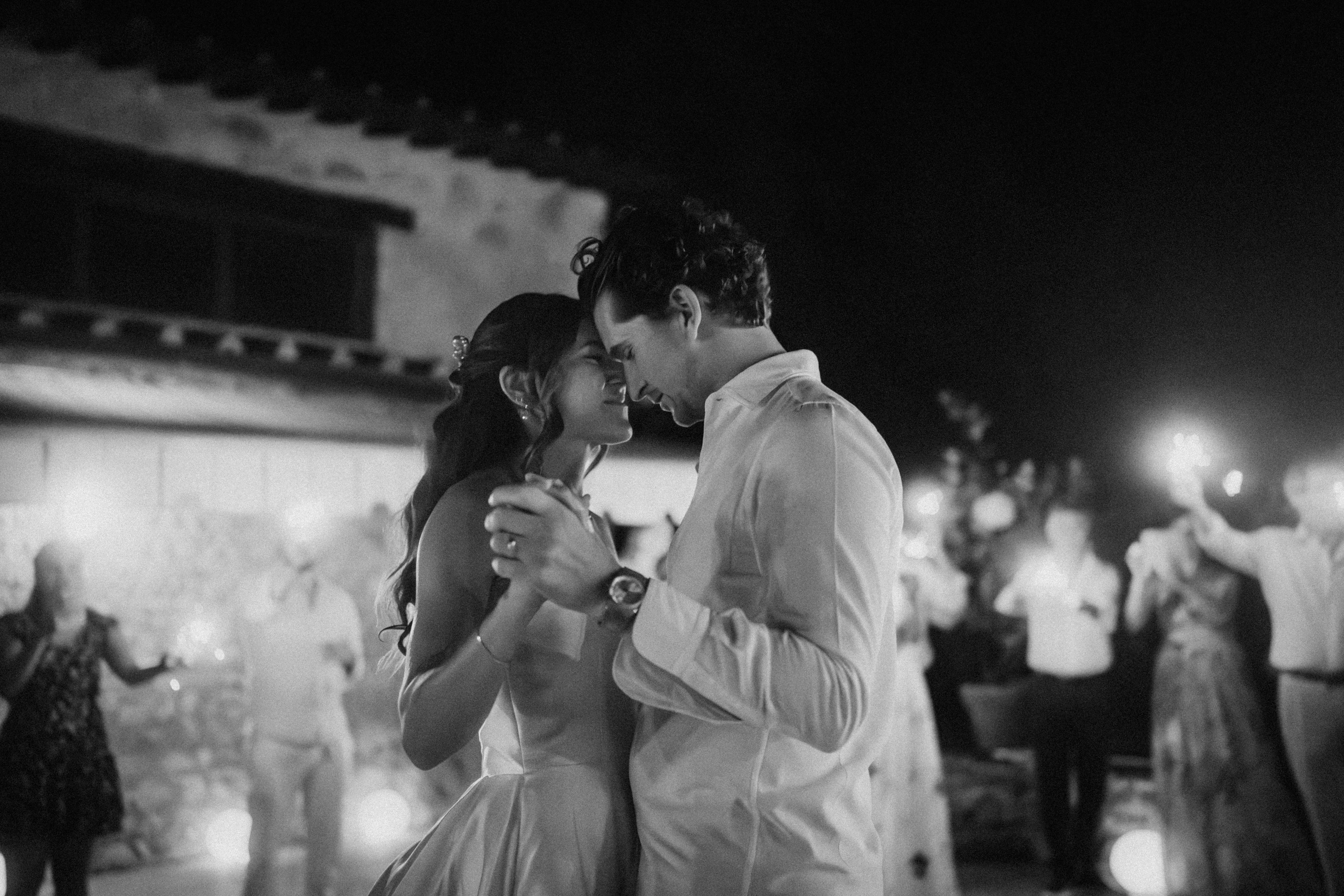 Inniger Hochzeitstanz unter freiem Himmel bei Nacht: Das Paar tanzt verliebt, im Hintergrund Gäste mit Wunderkerzen.