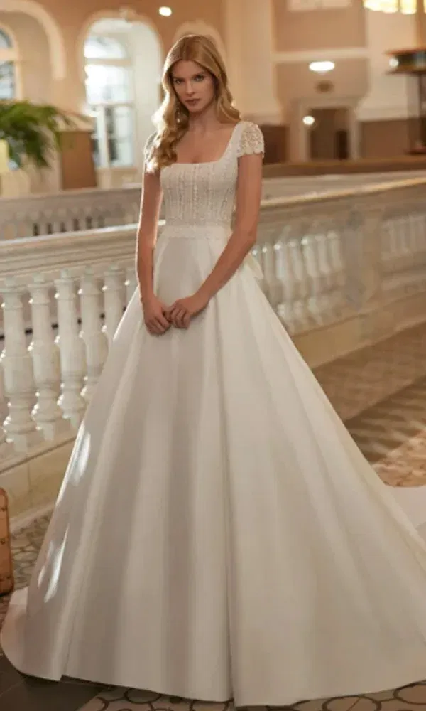 Elegantes Hochzeitskleid mit weitem Rock und filigraner Spitze am Oberteil, inszeniert vor einem historischen Treppenhaus.