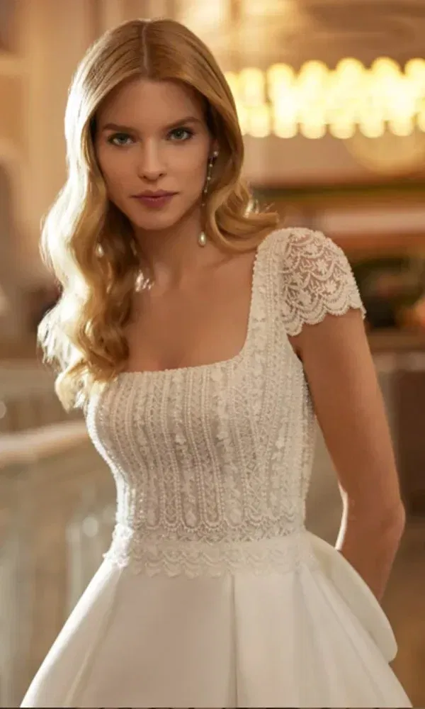Nahaufnahme einer Braut mit welligem Haar im eleganten Kleid mit Spitzenmieder und angeschnittenen Spitzenärmeln.