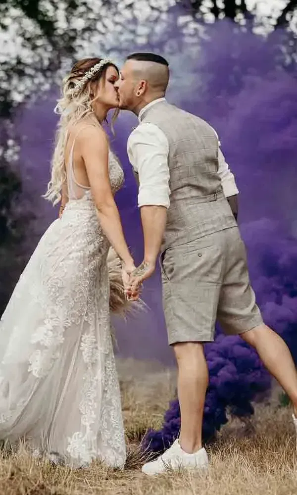 Stimmungsvolles Hochzeitsfoto mit violetter Rauchbombe – die Braut im Spitzenkleid hält den Bräutigam an der Hand.