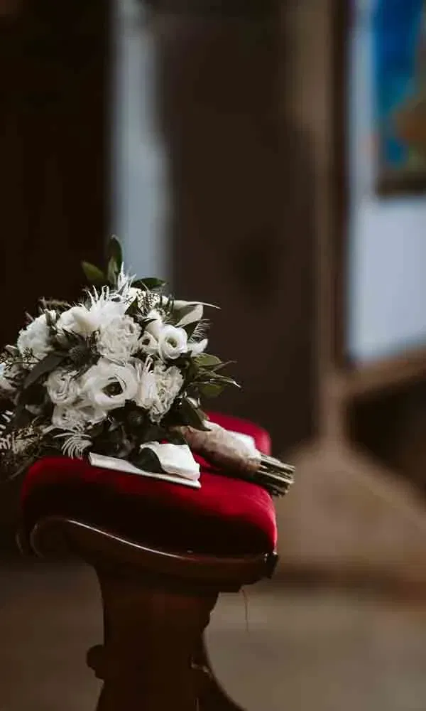 Eleganter Blumenstrauß mit Weiß- und Grüntönen, dekorativ auf einem Samthocker in der Kirche platziert.