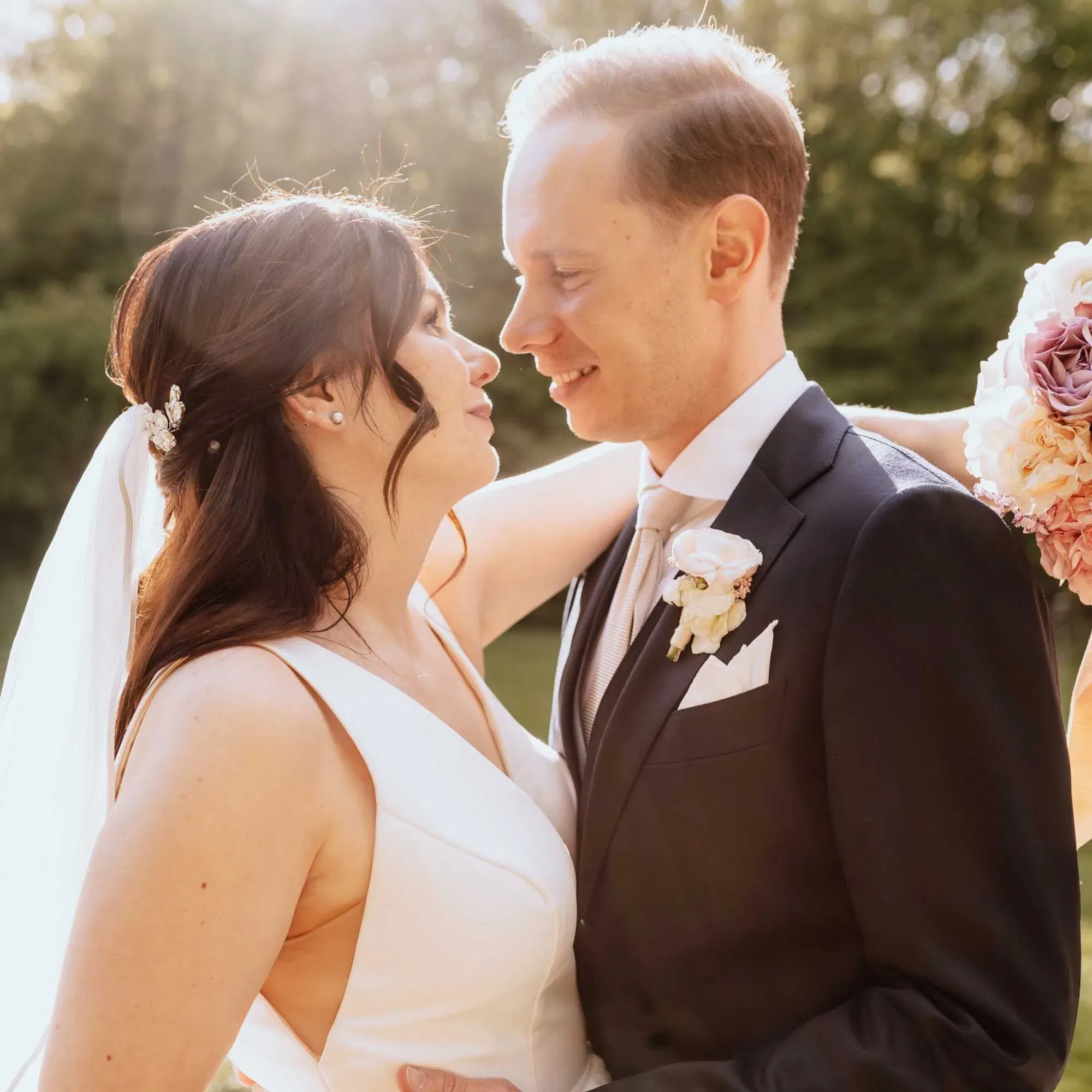Ein inniger Moment zwischen Braut und Bräutigam im Sonnenlicht – sie schauen sich tief in die Augen, umgeben von Natur.