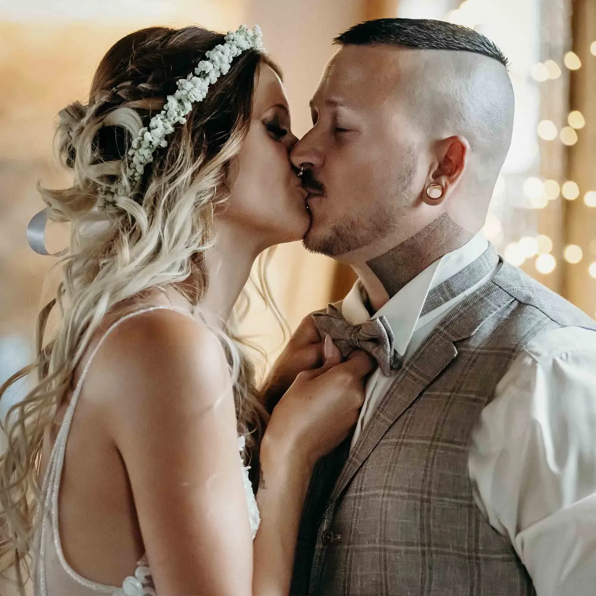 Inniger Kuss eines frisch vermählten Paares – die Braut mit offenen Haaren und Blütenschmuck, der Bräutigam in grauer Anzugweste.