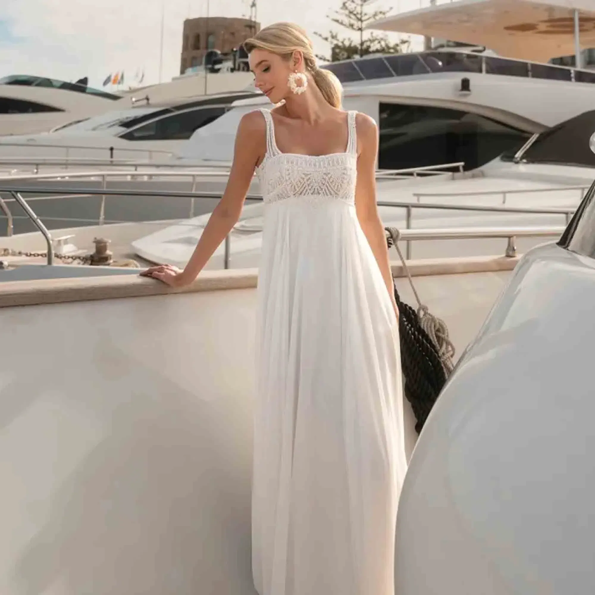 Leichtes Sommer-Brautkleid mit hoher Taille und Spitzenbustier – aufgenommen an Deck zwischen weißen Yachten.