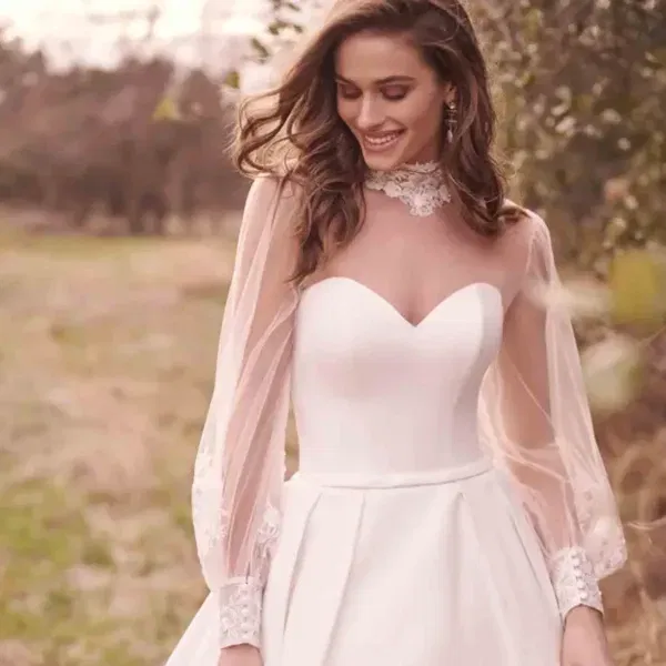 Braut in einem eleganten Ballkleid mit Herzausschnitt und zarten Tüllärmeln, verziert mit Spitze, posiert auf einer Wiese.