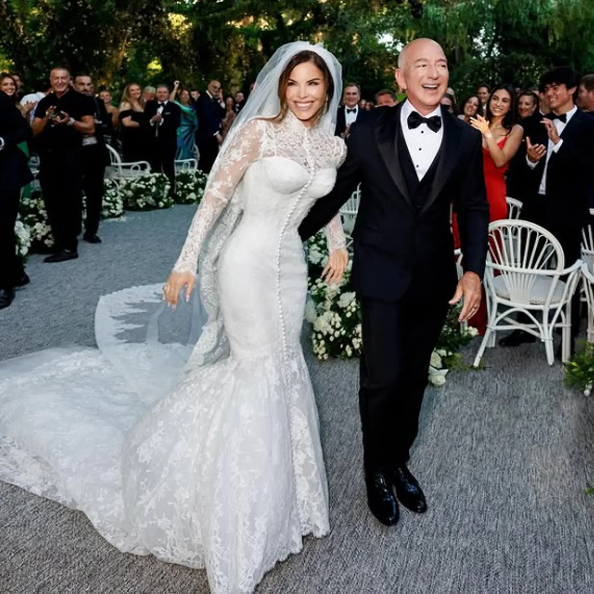 Elegantes Hochzeitspaar bei der Trauung im Freien – die Braut trägt ein langärmeliges, eng anliegendes Brautkleid mit Spitze und langer Schleppe.