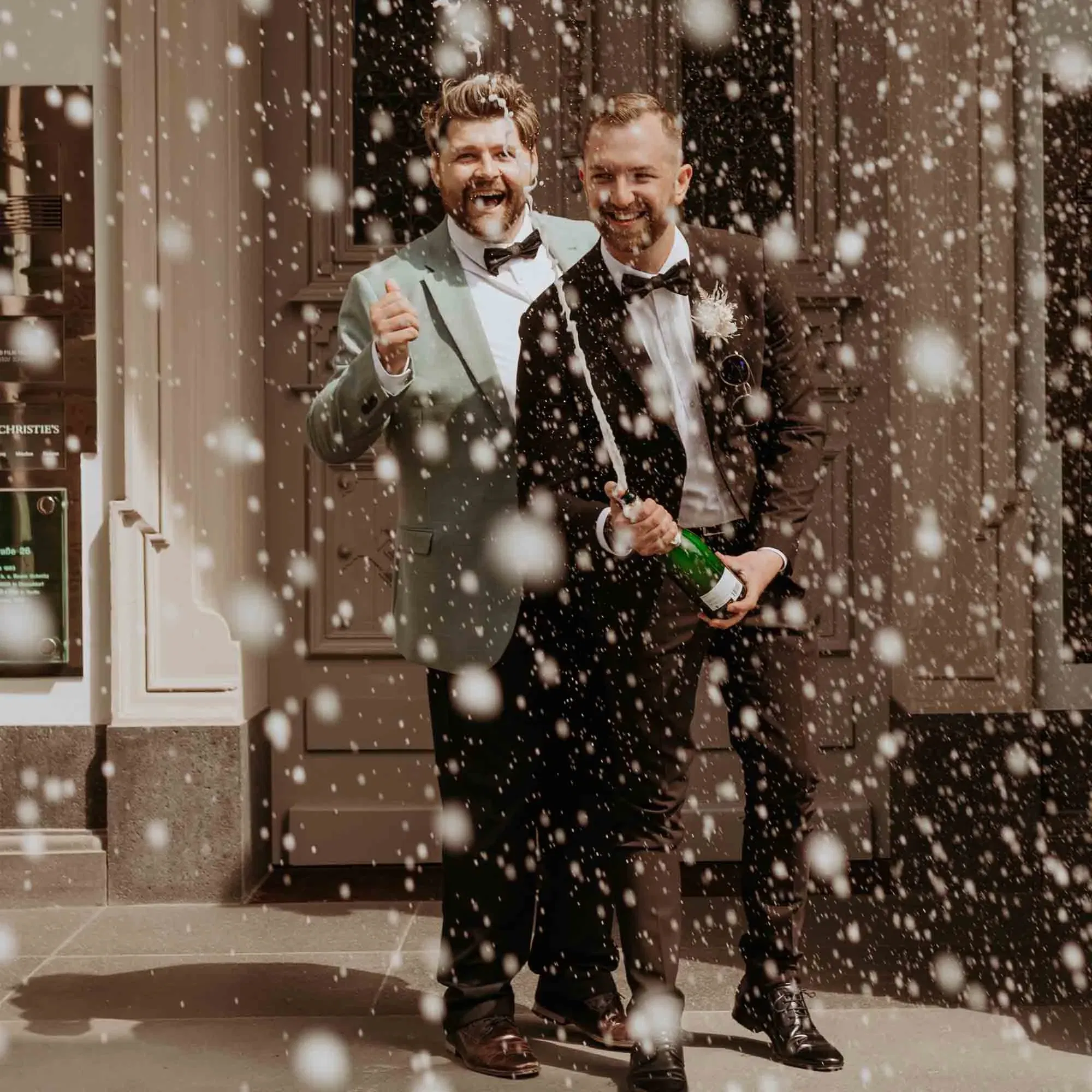 Glückliches Hochzeitspaar stößt draußen mit Champagner an, funkelnde Tropfen umgeben sie in festlicher Stimmung.