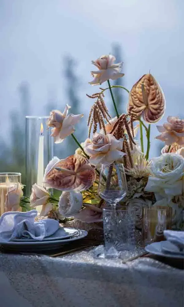 Elegante Blumendekoration in Beige- und Rosétönen mit edlen Gläsern und gedecktem Geschirr.
