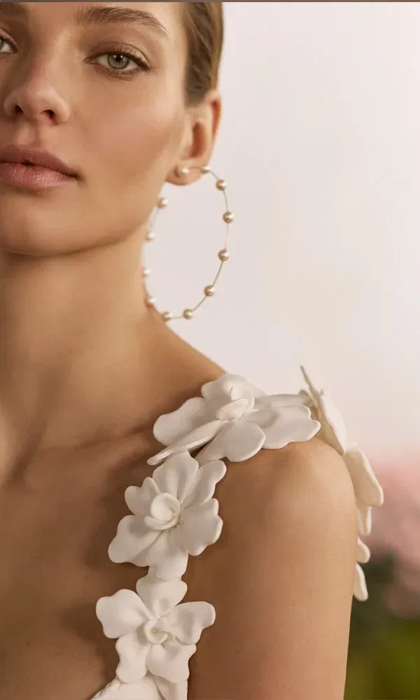Detail eines Hochzeitskleids mit kunstvollen Stoffblüten auf den Trägern und dezenter, natürlicher Braut-Make-up.