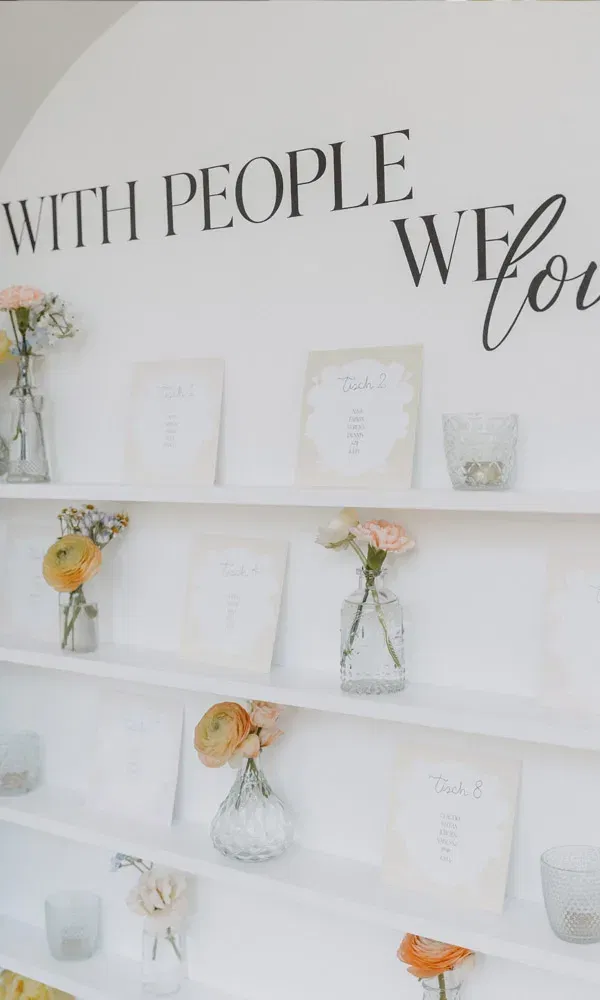 Sitzplan-Wand zur Hochzeit, dekoriert mit Karten der Tischnummern, kleinen Vasen mit Blumen und Teelichthaltern.