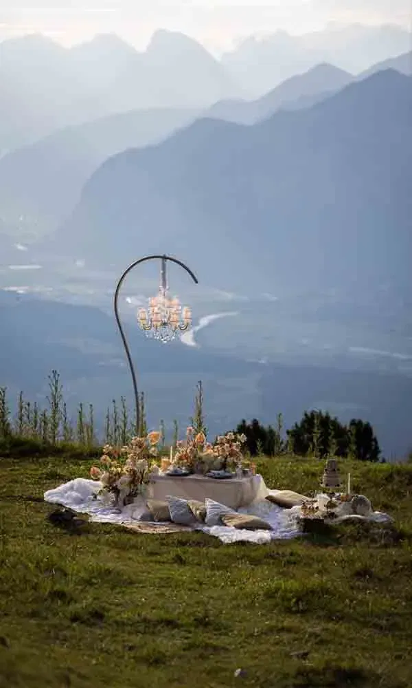 Festlich dekoriertes Picknick mit Kissen, Tafel und floraler Deko hoch oben in den Alpen.