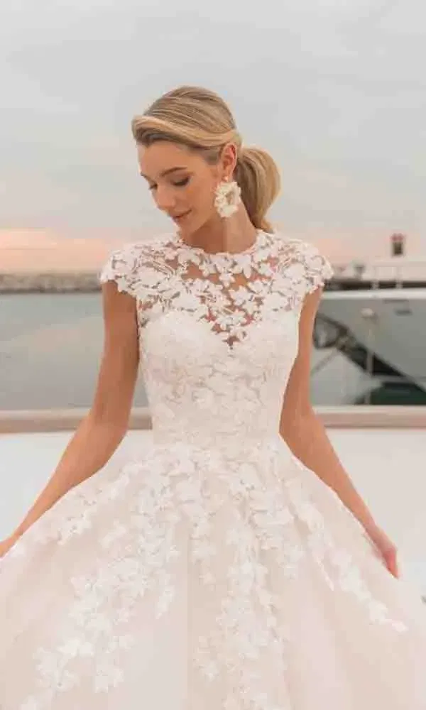 Brautkleid mit hochgeschlossenem Spitzenoberteil und eleganten Spitzenornamenten in maritimer Kulisse.